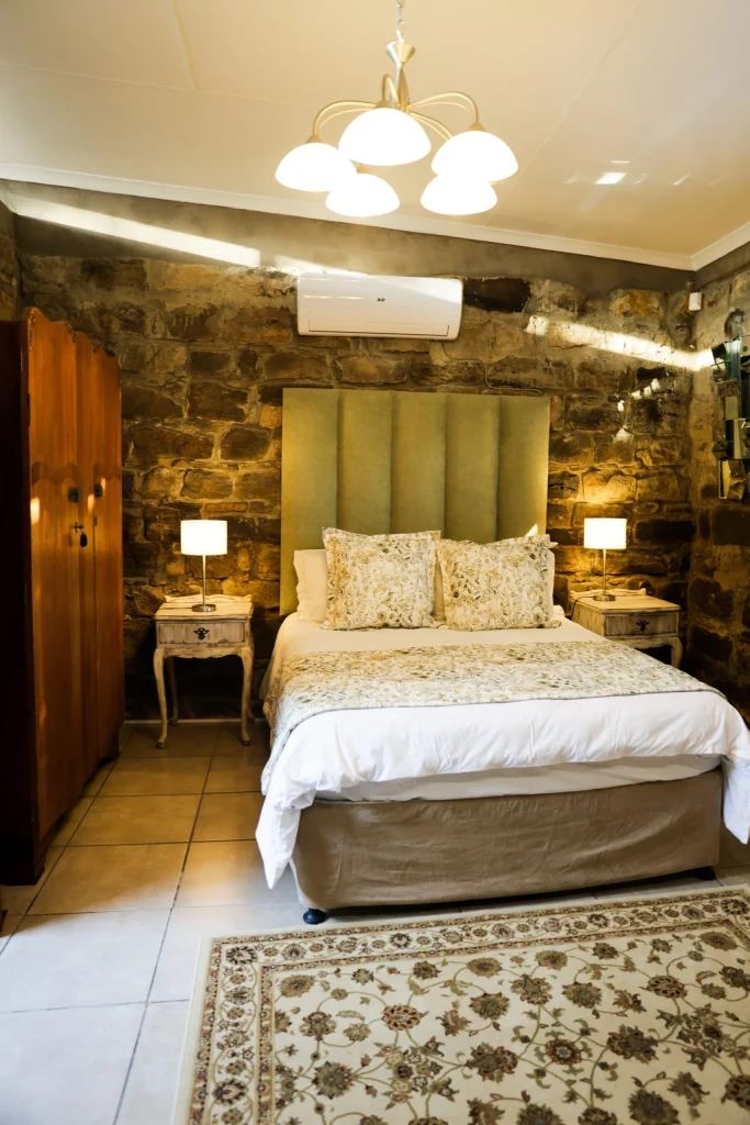 Comfortable guest room with a queen bed, large green pillows, framed bird prints, and soft lighting from matching bedside lamps.