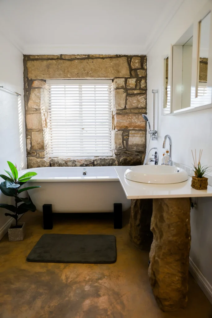 Rustic-style bathroom featuring a stone wall, modern toilet and basin, and natural light from a window with blinds.