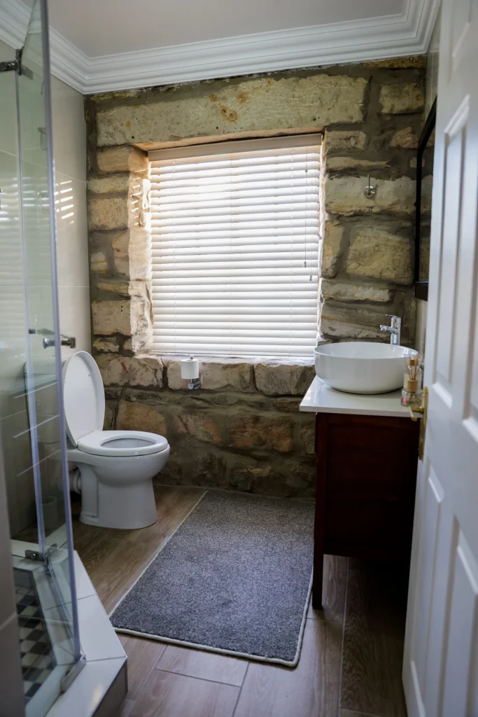 Inviting bathroom with a freestanding bathtub, stone-framed window, stone pillar sink, and green plant accent.