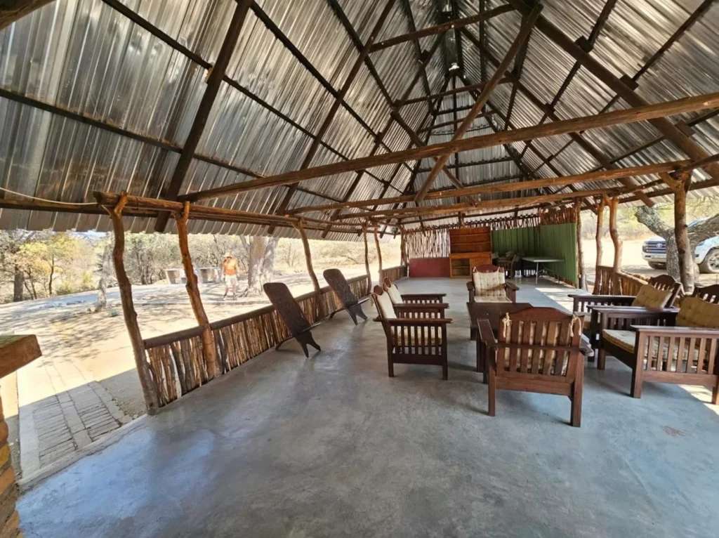 Open-air communal lounge area in a Botswana safari camp with wooden furniture under a high thatched roof.